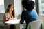Two women sit across a table talking to each other