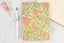 A floral bullet journal notebook on a white table next to a white pen.