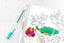 A colorful coloring book page with flowers on it and two pens next to it.