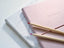 A pink notebook on top of a white notebook, with two colored pencils on top