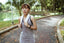 A woman walks down a park path in workout clothes with a towel over her shoulders