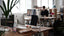 A person works at a desk in an office with many desks and plants