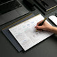 Person writing in a planner with a laptop and office supplies on a desk