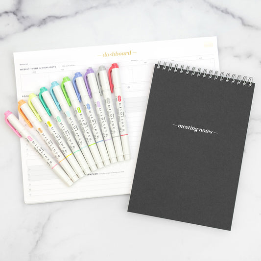 Set of colorful markers and a black notebook on a marble surface