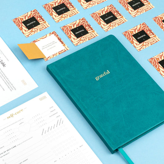 Teal notebook with 'grateful' on a blue background with cards and papers.